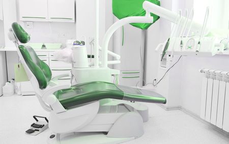 A green dental chair is sitting in a dental office.