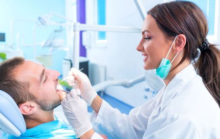 A female dentist is examining a man 's teeth in a dental office.