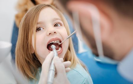 A little girl is getting her teeth examined by a dentist.