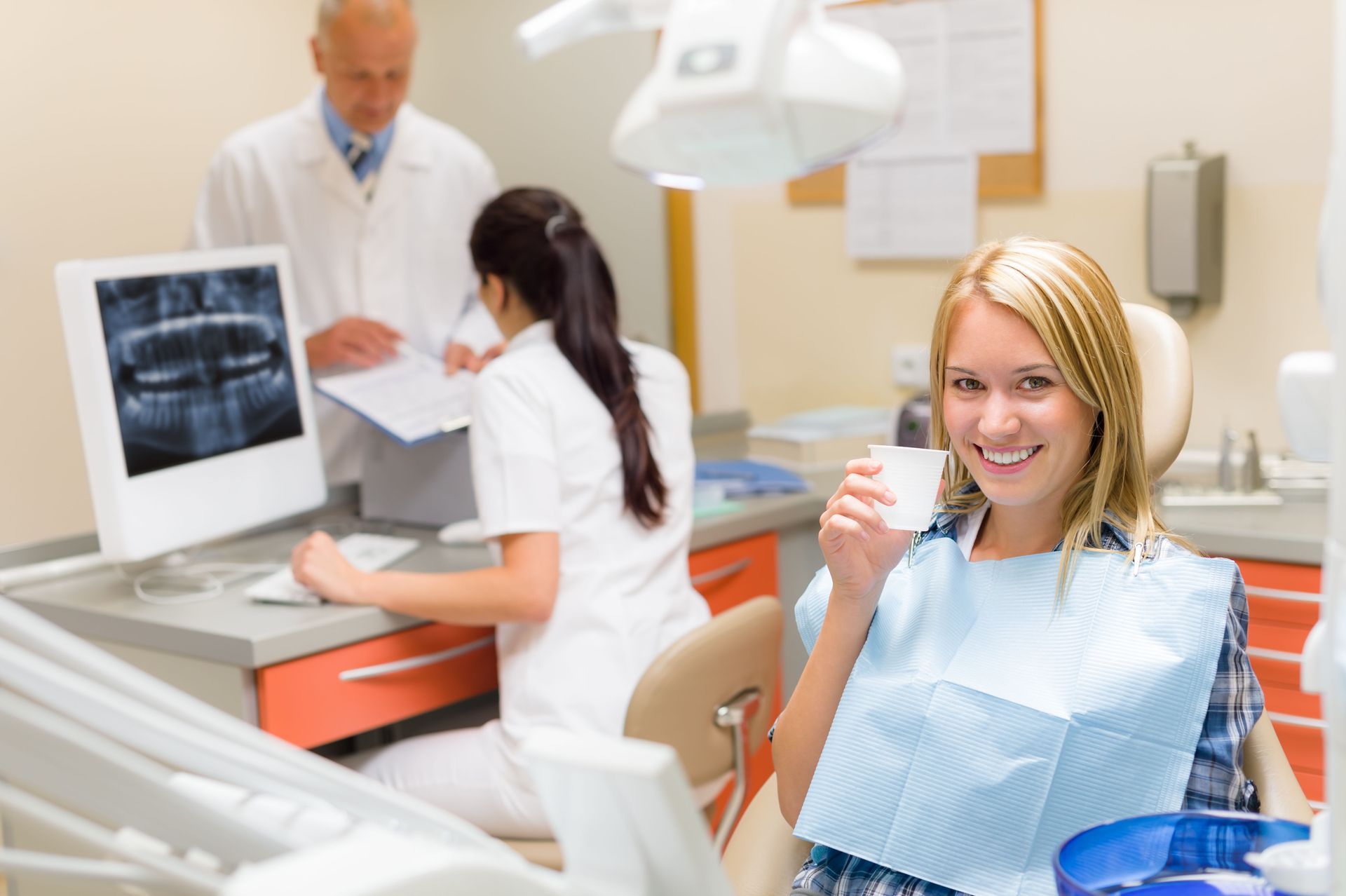 A woman is sitting in a dental chair holding a cup of coffee.
