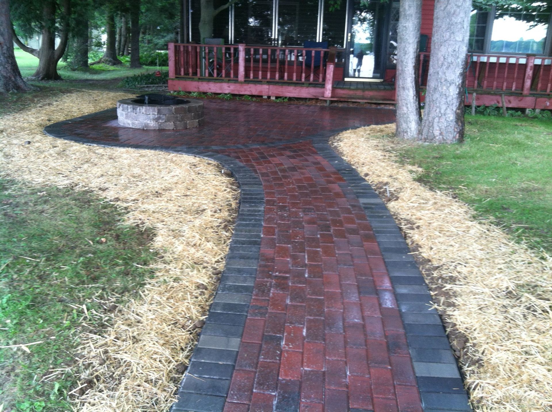 Brick garden walkway curving through grass toward a wooden deck under trees