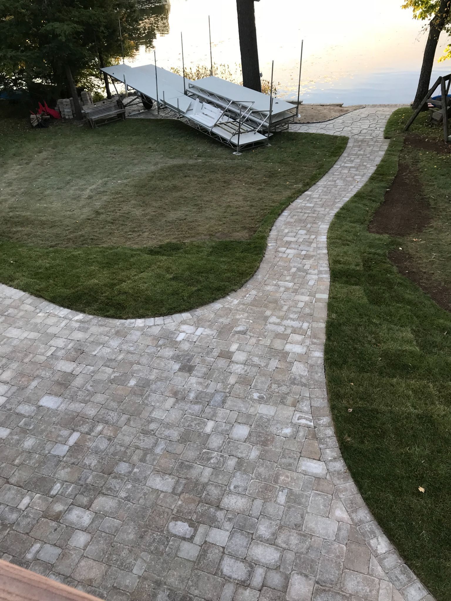 Curved stone path through grass to lakeside benches at sunset