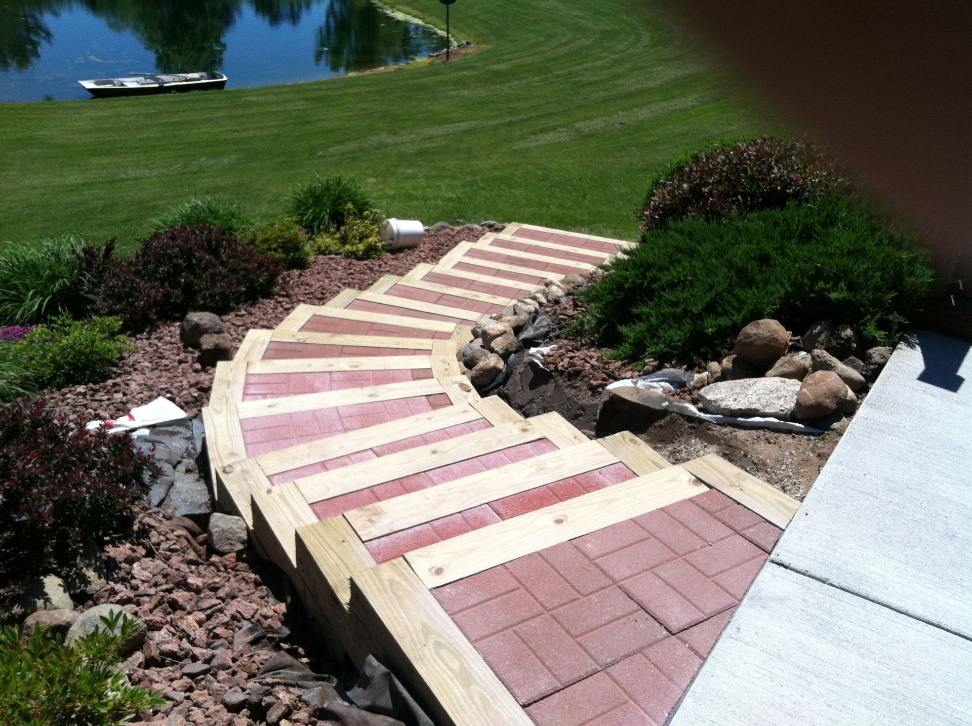 Curved brick-and-stone garden steps descending beside rocks and shrubs toward a grassy lawn and pond