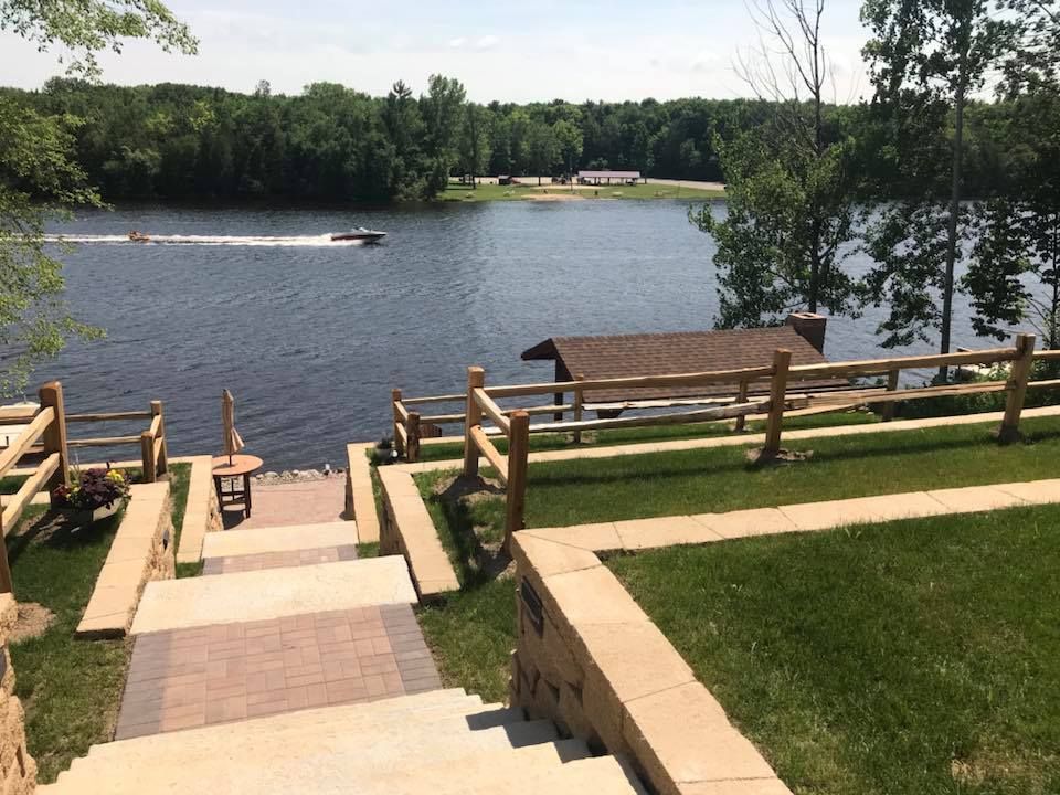 Lakeside walkway and steps leading to a dock on a calm lake, with trees and lawn around it