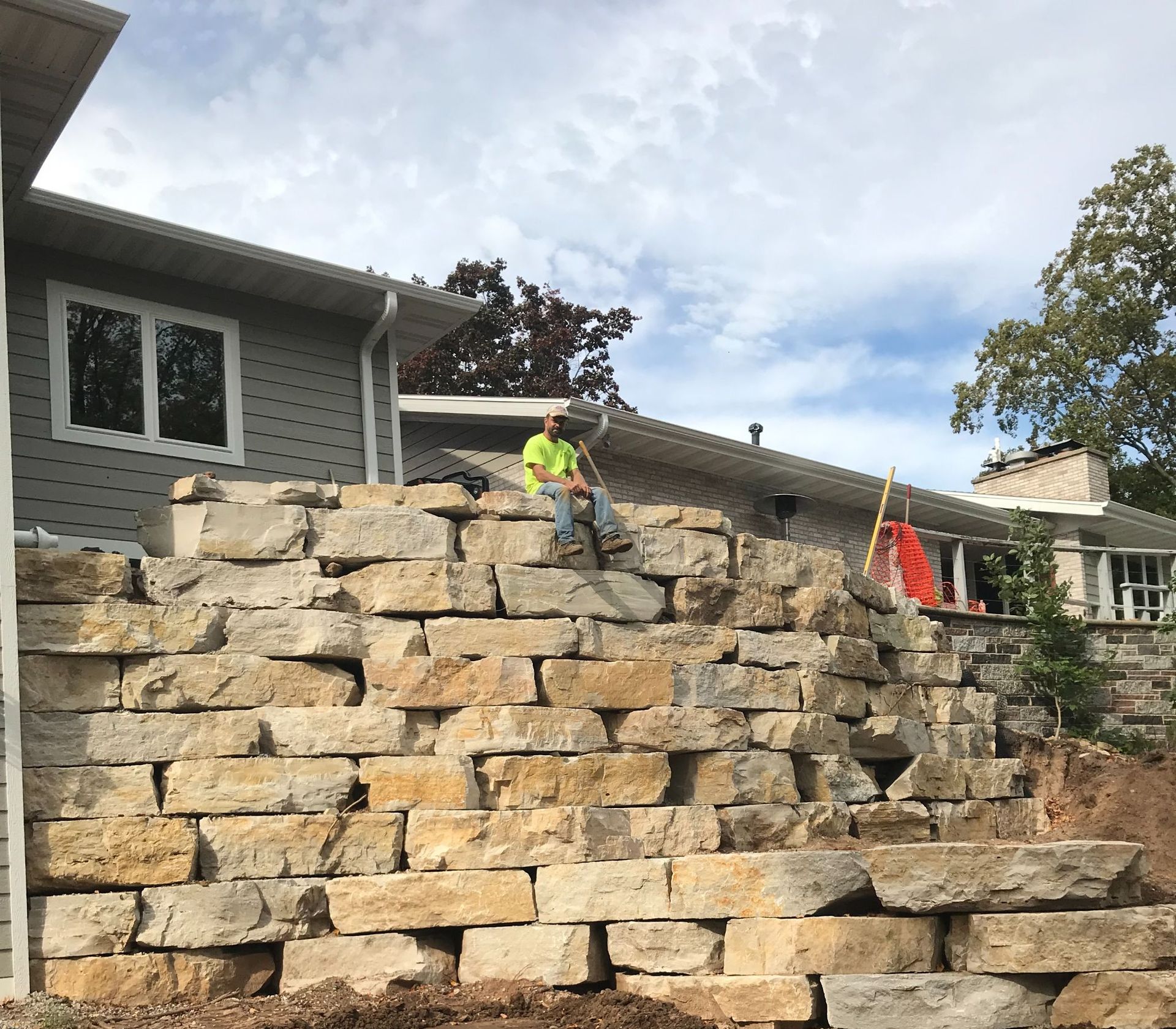 Worker in neon vest on stacked stone retaining wall at a residential construction site