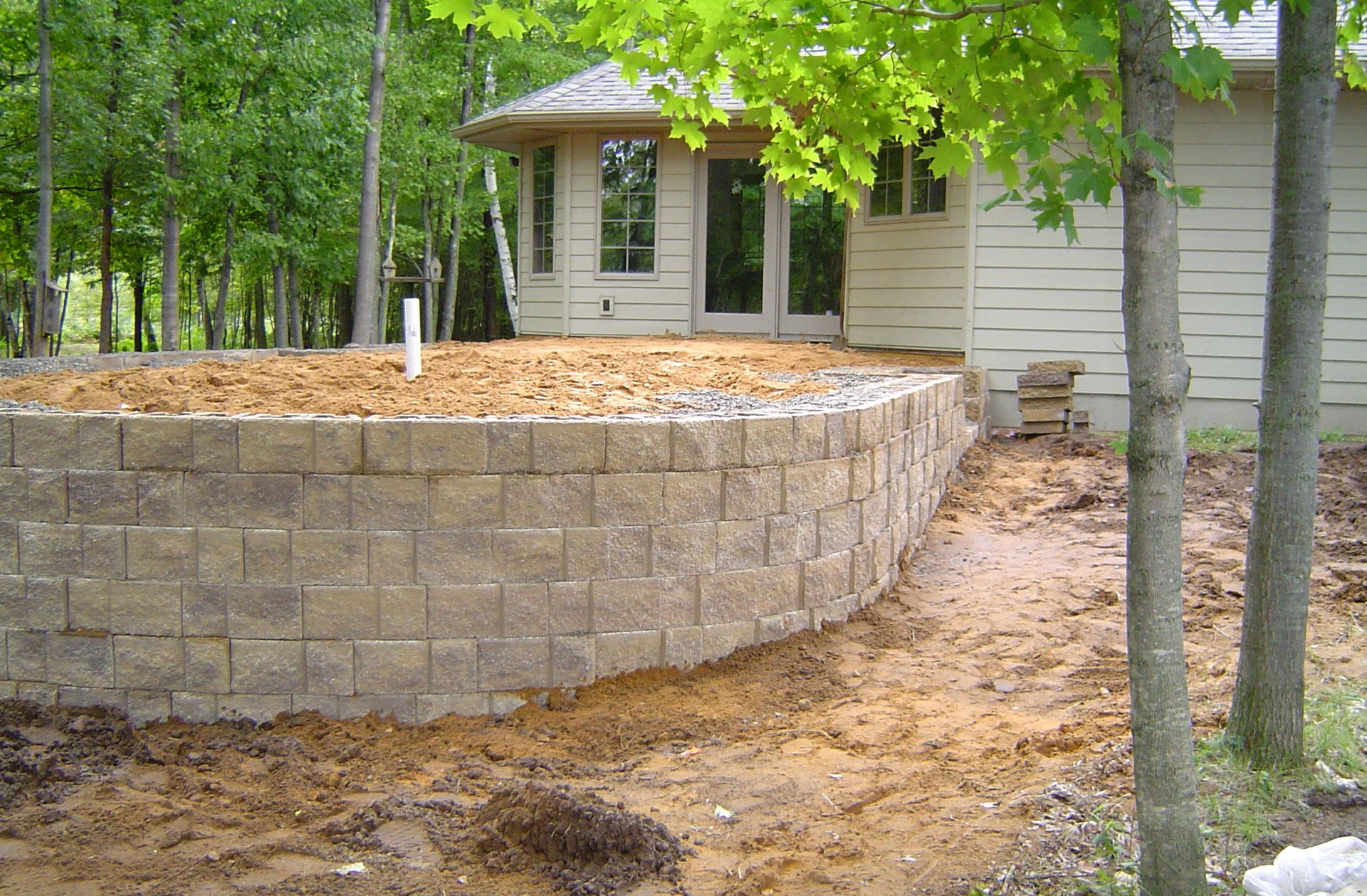 Stone retaining wall and bare landscaping beside a house in a wooded yard