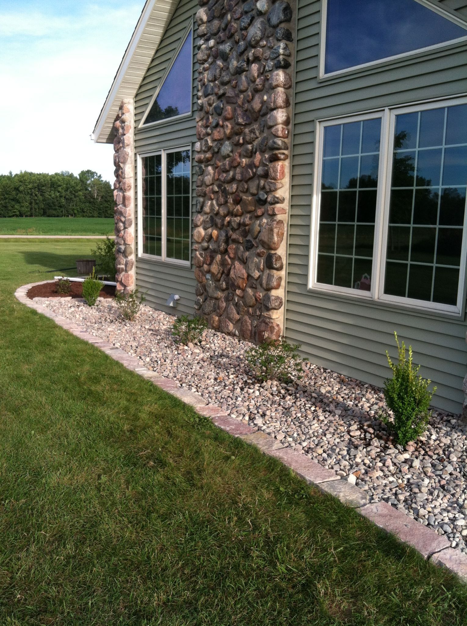 House exterior with stone chimney, gray siding, and white landscaping rock border along the lawn