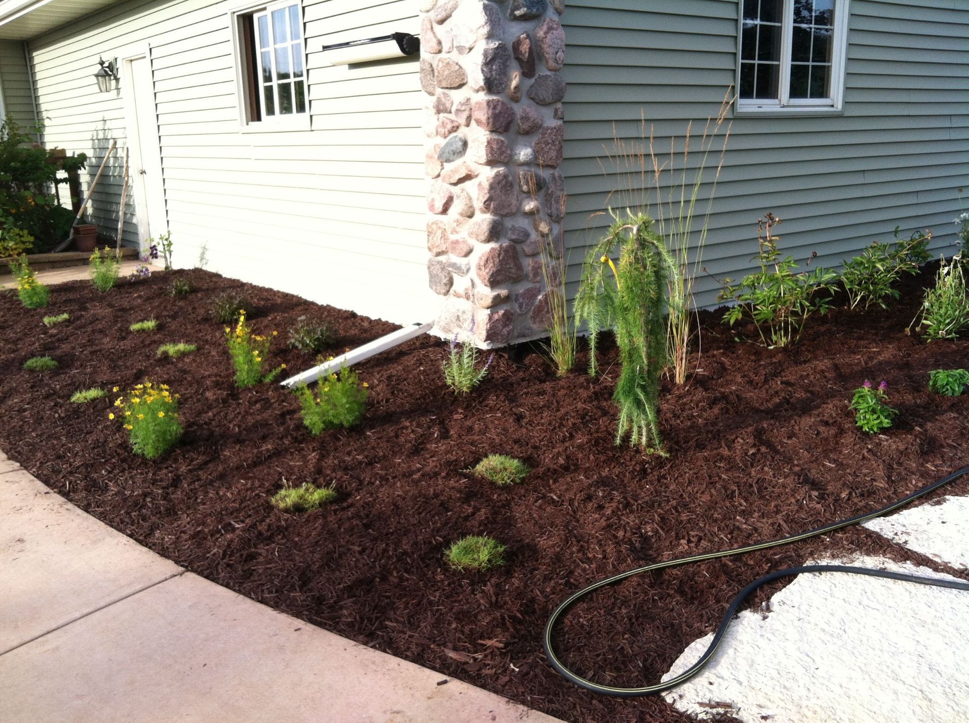 Freshly landscaped front yard with dark mulch, small shrubs, and a stone house exterior
