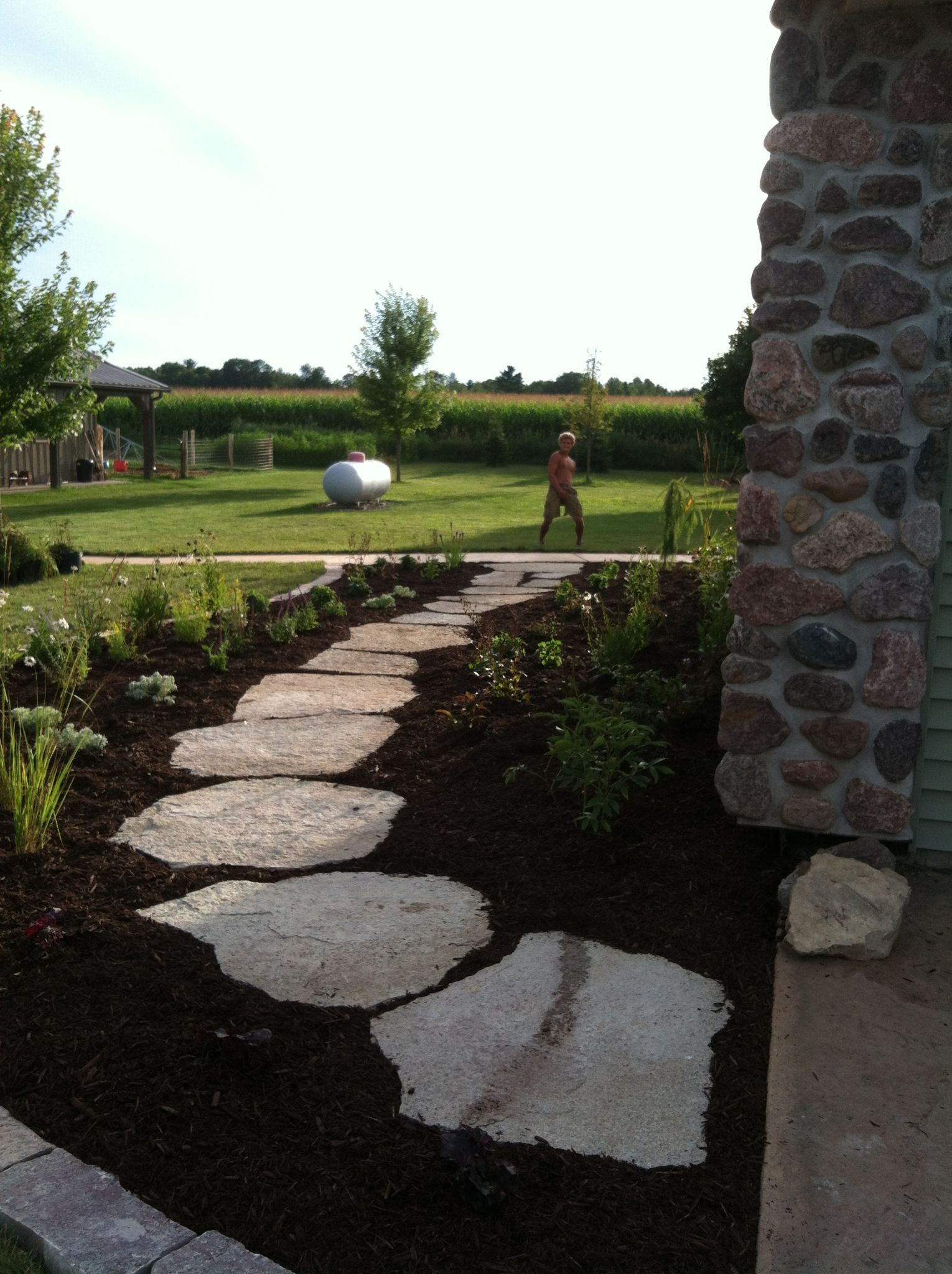 Stone garden path beside a lawn, with a child near a large silver ball in the distance.