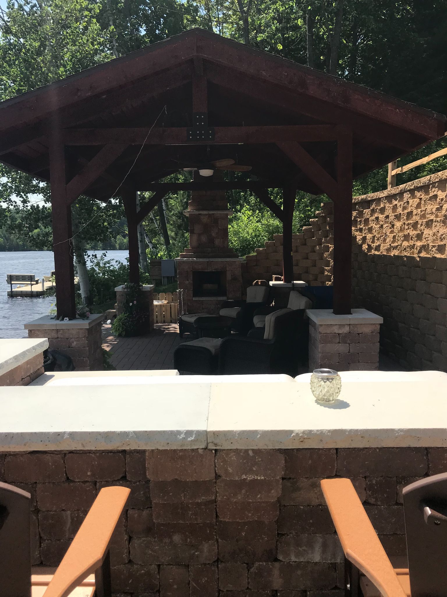 Outdoor pavilion with stone grill, wooden beams, and poolside seating under trees