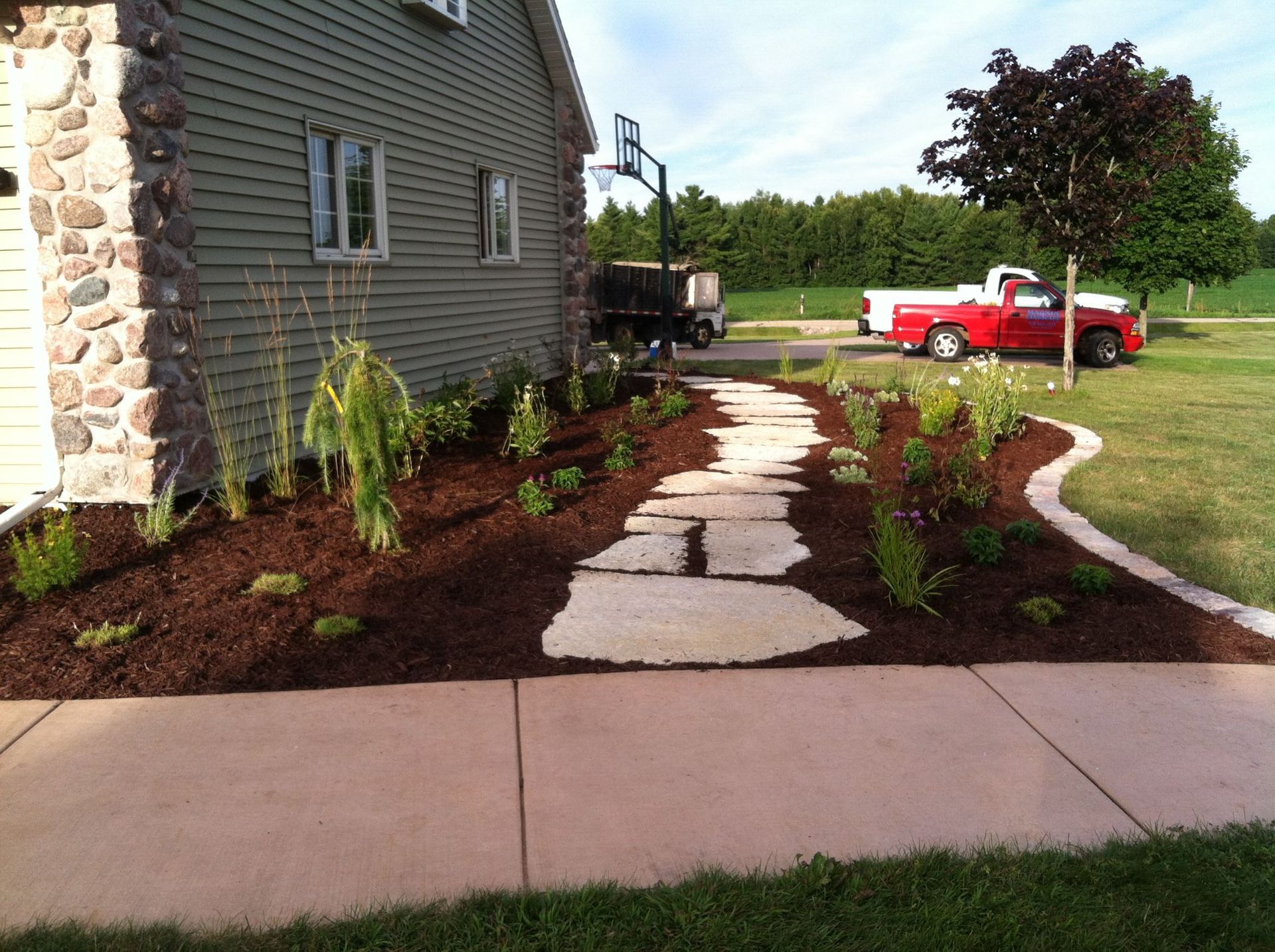 Stone house garden path with young plants, a red truck, and a lawn under bright sunlight