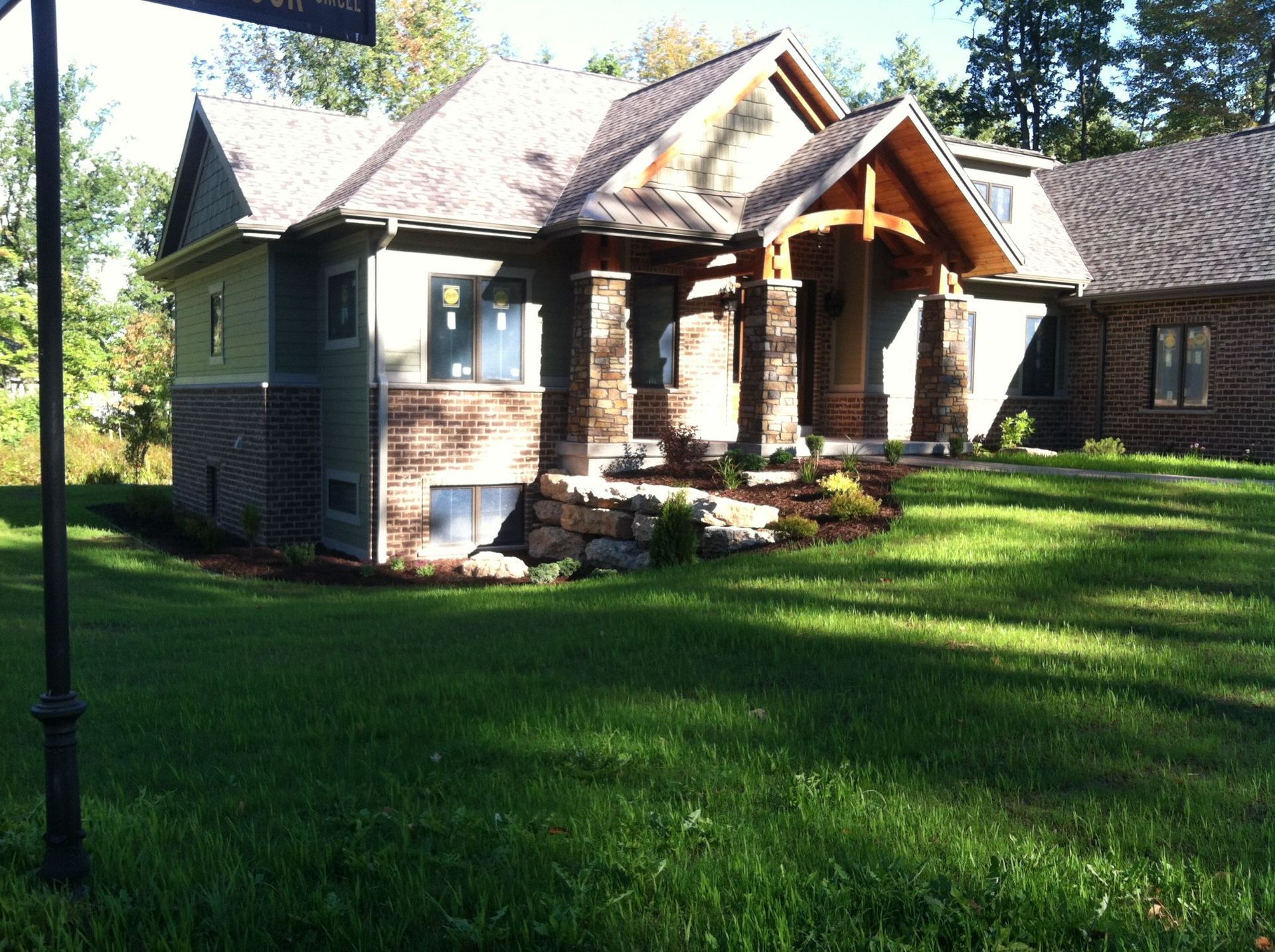 Small stone house with a covered porch and green lawn in sunlight.