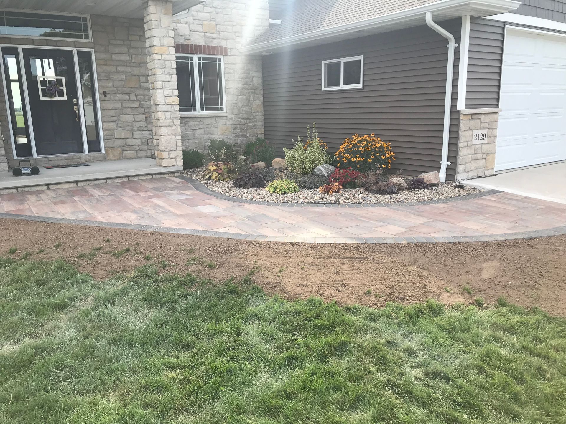 Front yard with curved paver walkway, stone entry, garage, and flower bed in front of a house