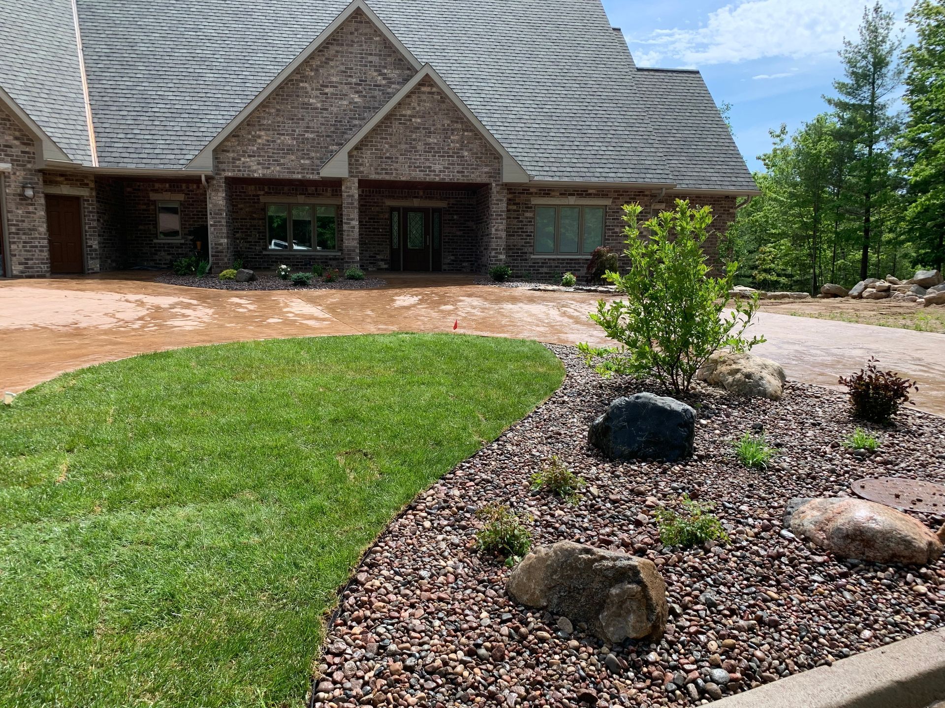 Landscaped front yard with curved lawn, rock bed, and a stone house with a steep roof