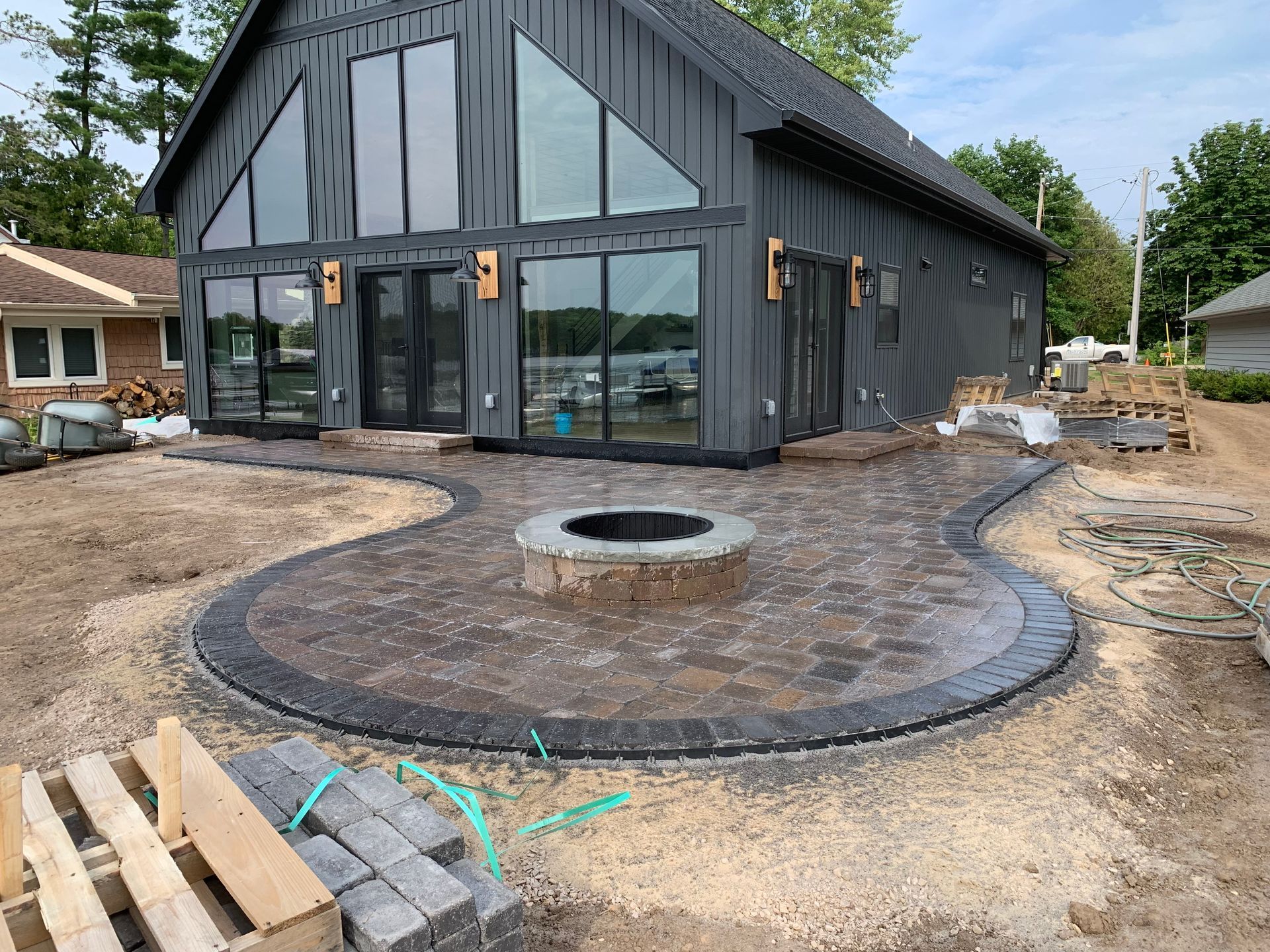 Modern black house with large glass doors and a circular patio/fire pit in a gravel yard