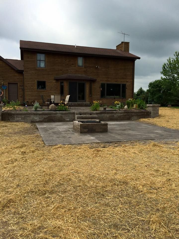 Wooden house with patio, stone fire pit, and straw-covered yard under cloudy skies
