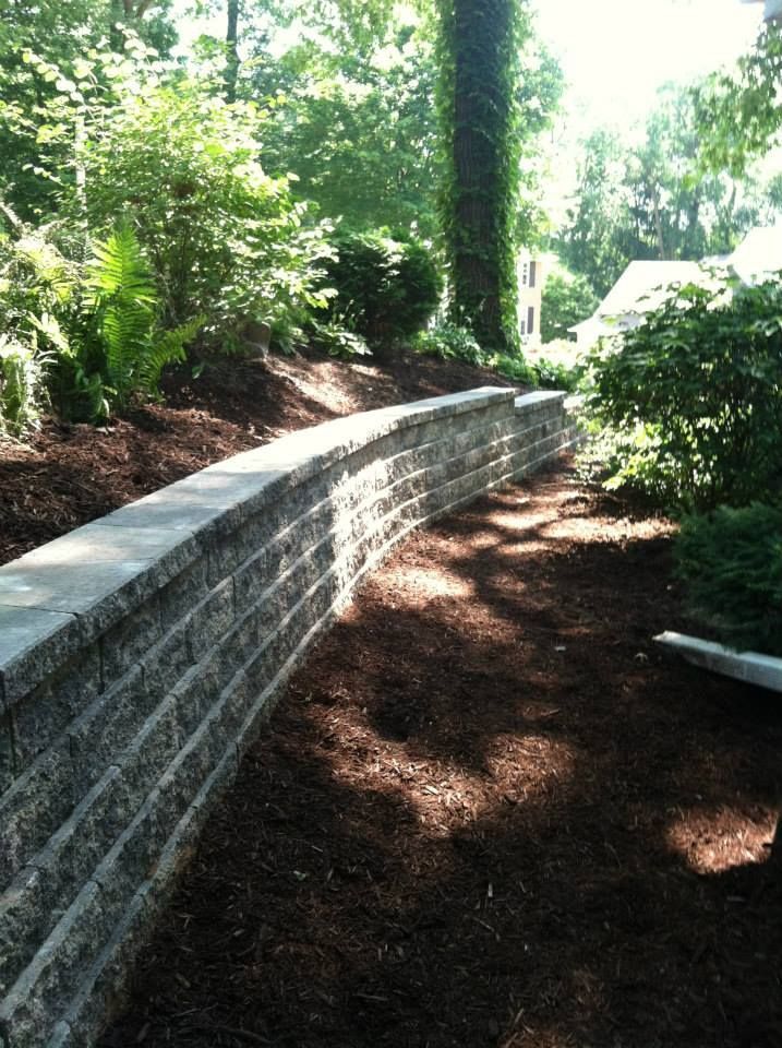 Curved stone retaining wall along a shaded garden path with trees and shrubs