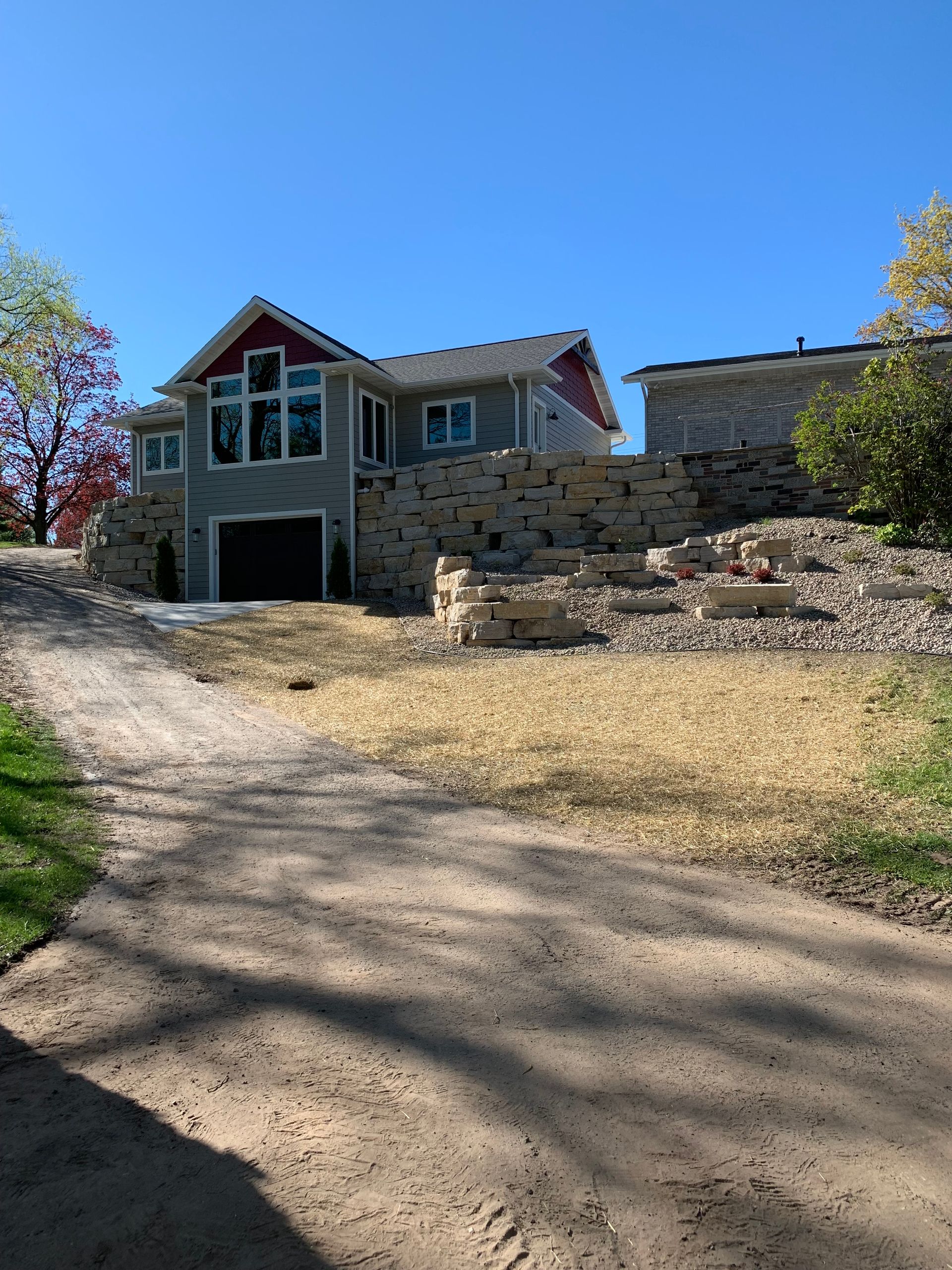 Stone house with a garage on a sloped dirt driveway under a clear blue sky
