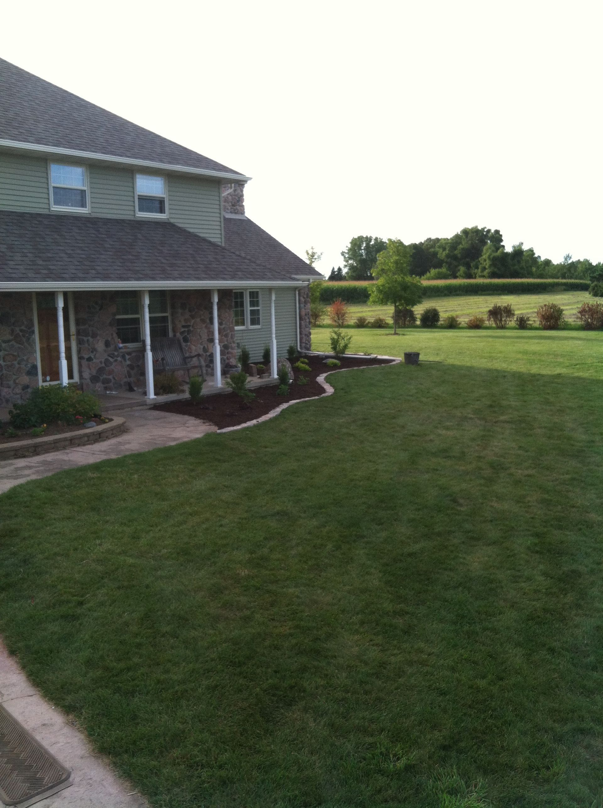 Suburban house with a front porch and a large green lawn under a bright sky