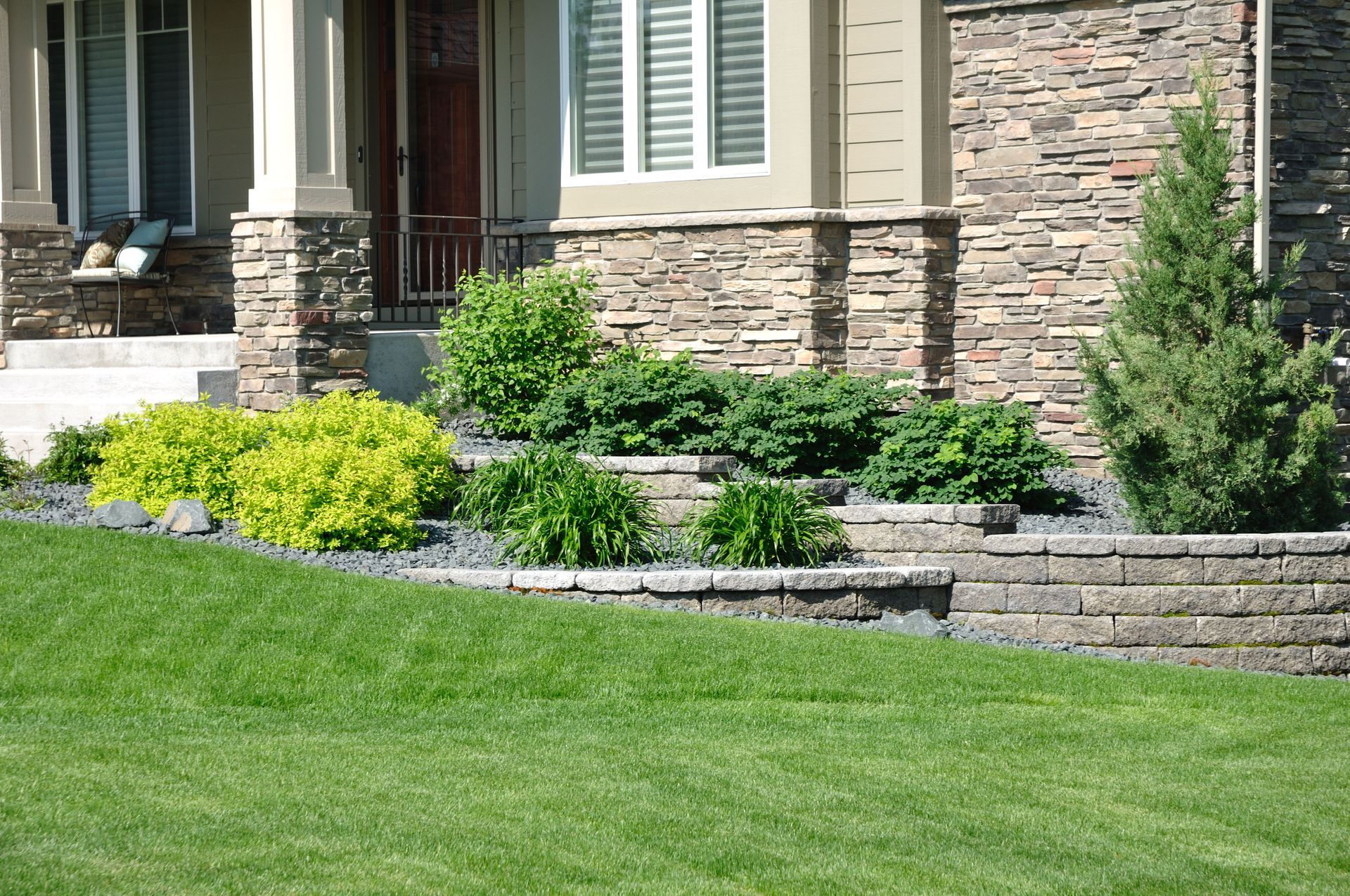 Front of a house with stone siding, low retaining wall, and landscaped flower beds along a green lawn