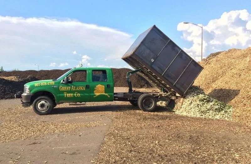 Green dump truck unloading a raised bed of mulch or wood chips in a sunny yard
