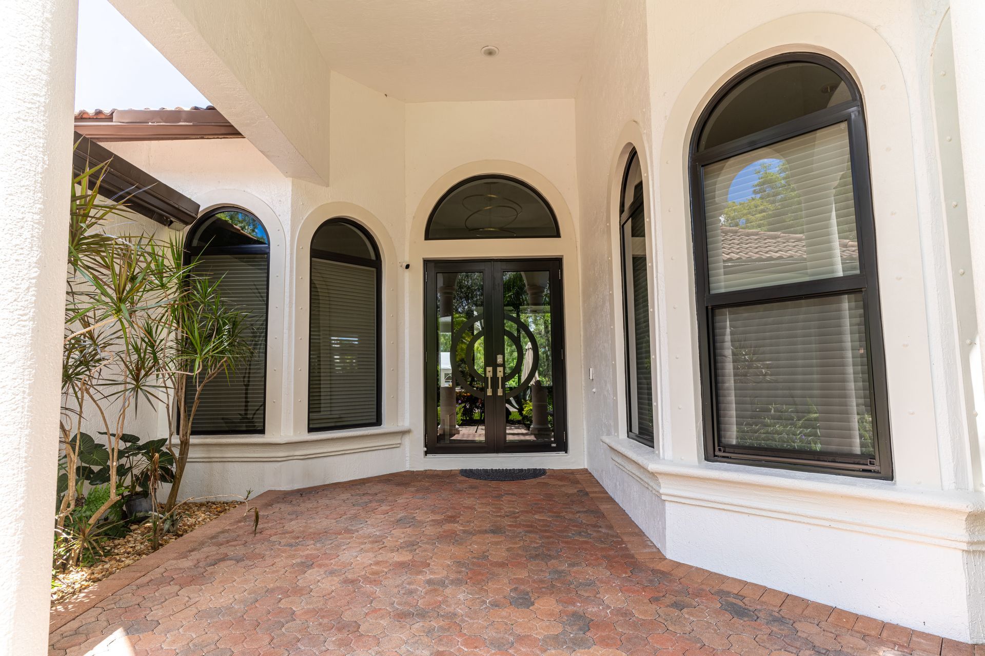 A white house with arched windows and a brick driveway leading to the front door.