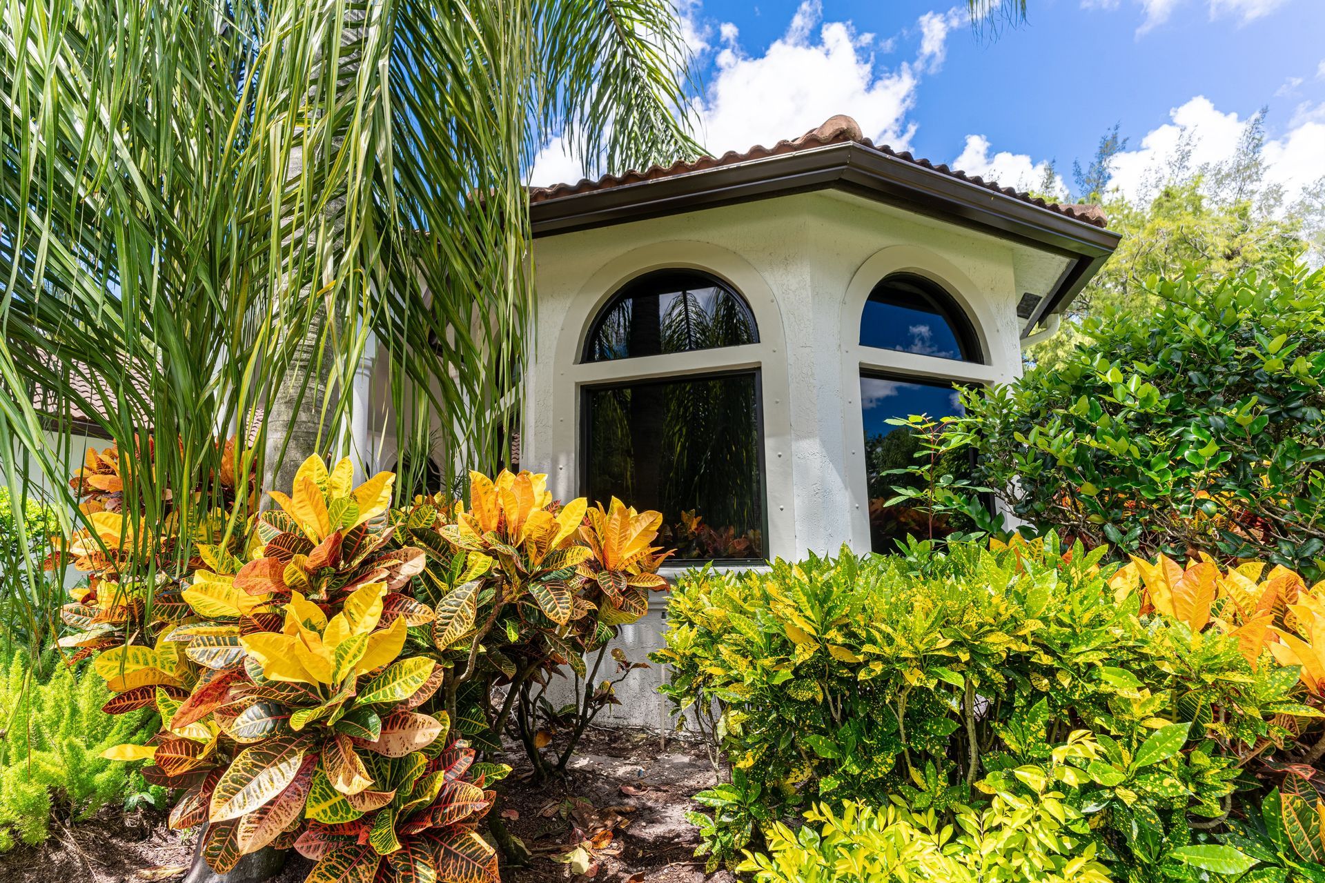 A white house with arched windows is surrounded by trees and bushes.