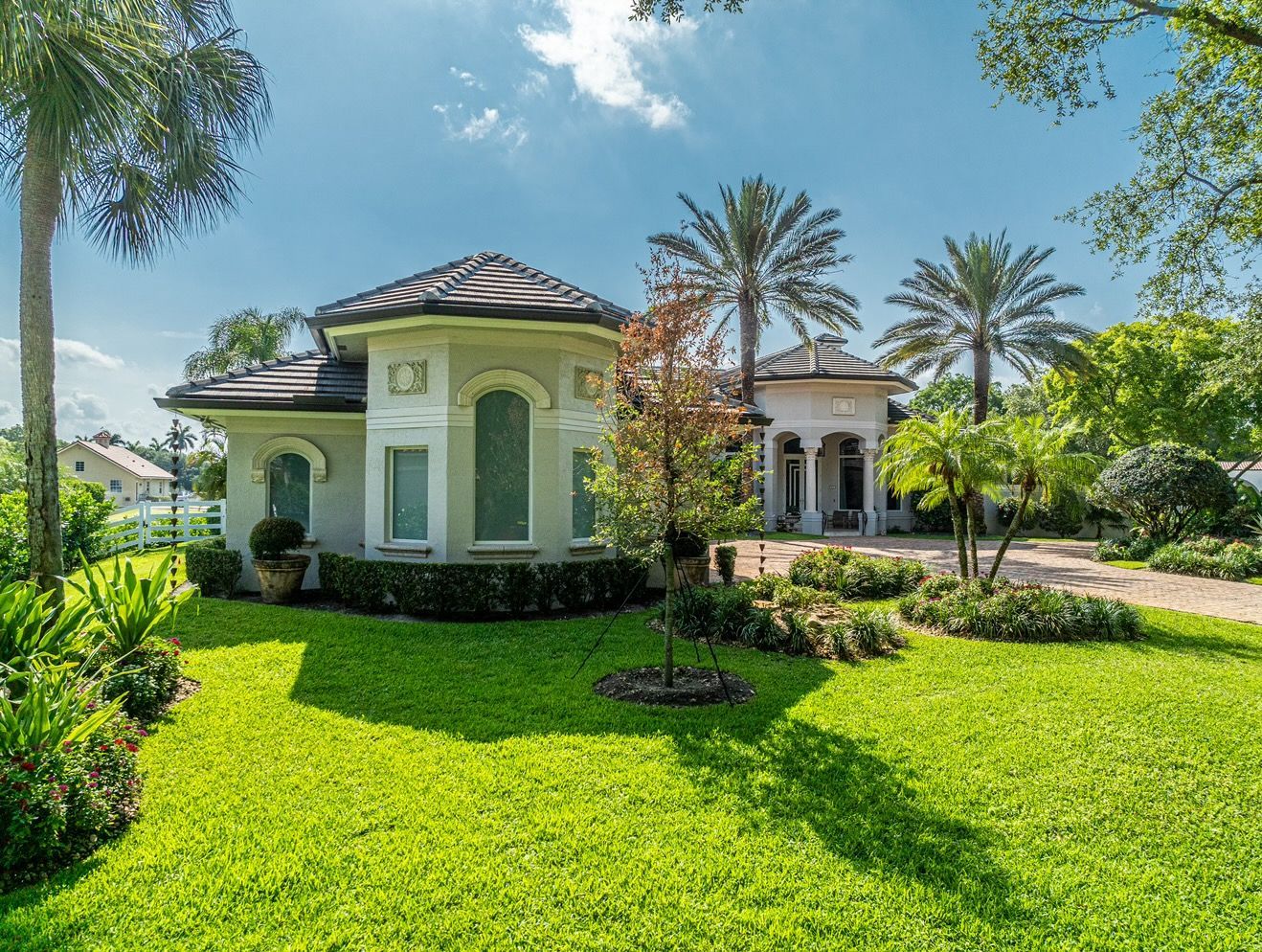 A white house with a lush green lawn and palm trees in front of it.