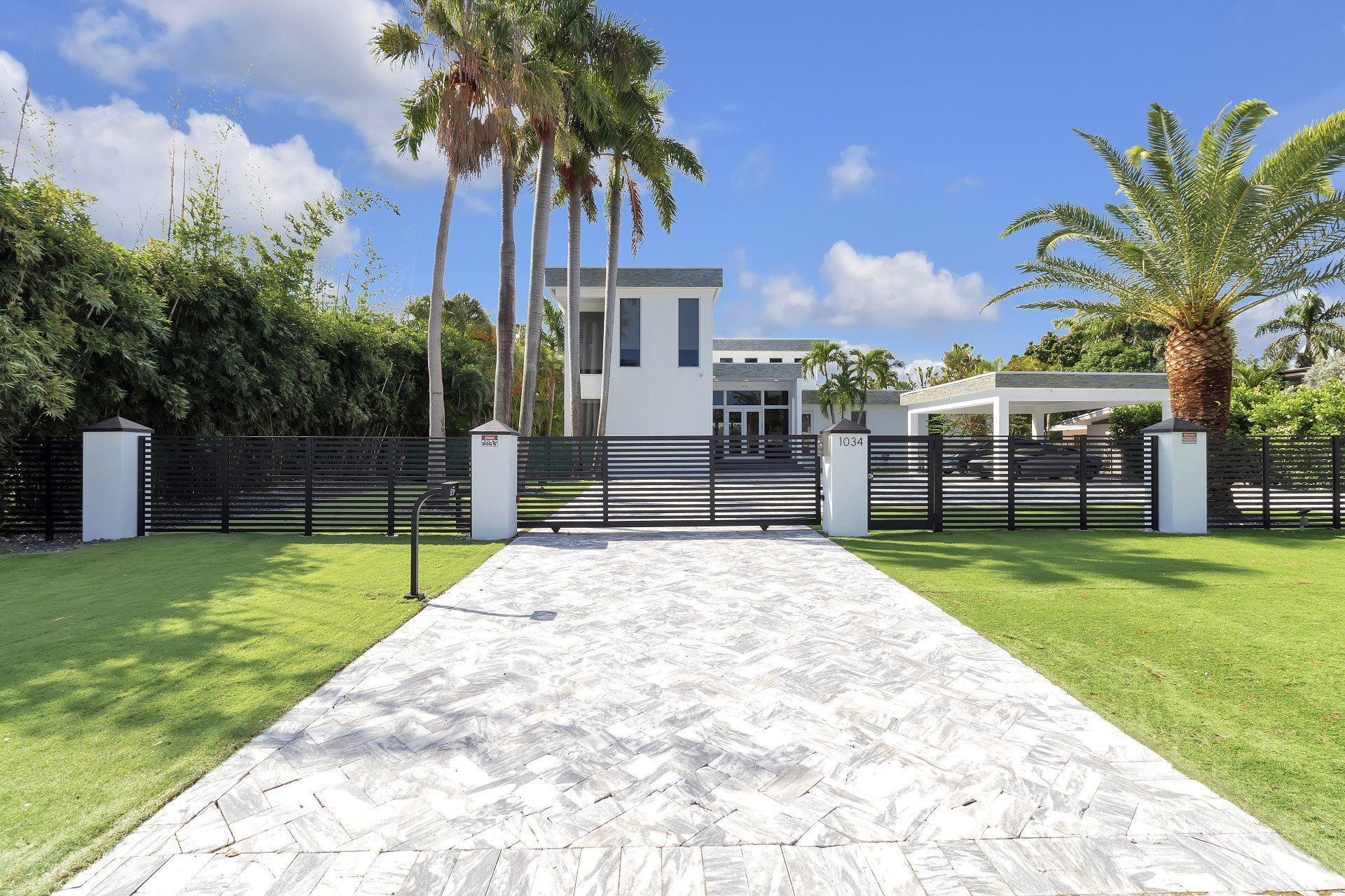 A driveway leading to a white house with palm trees in the background