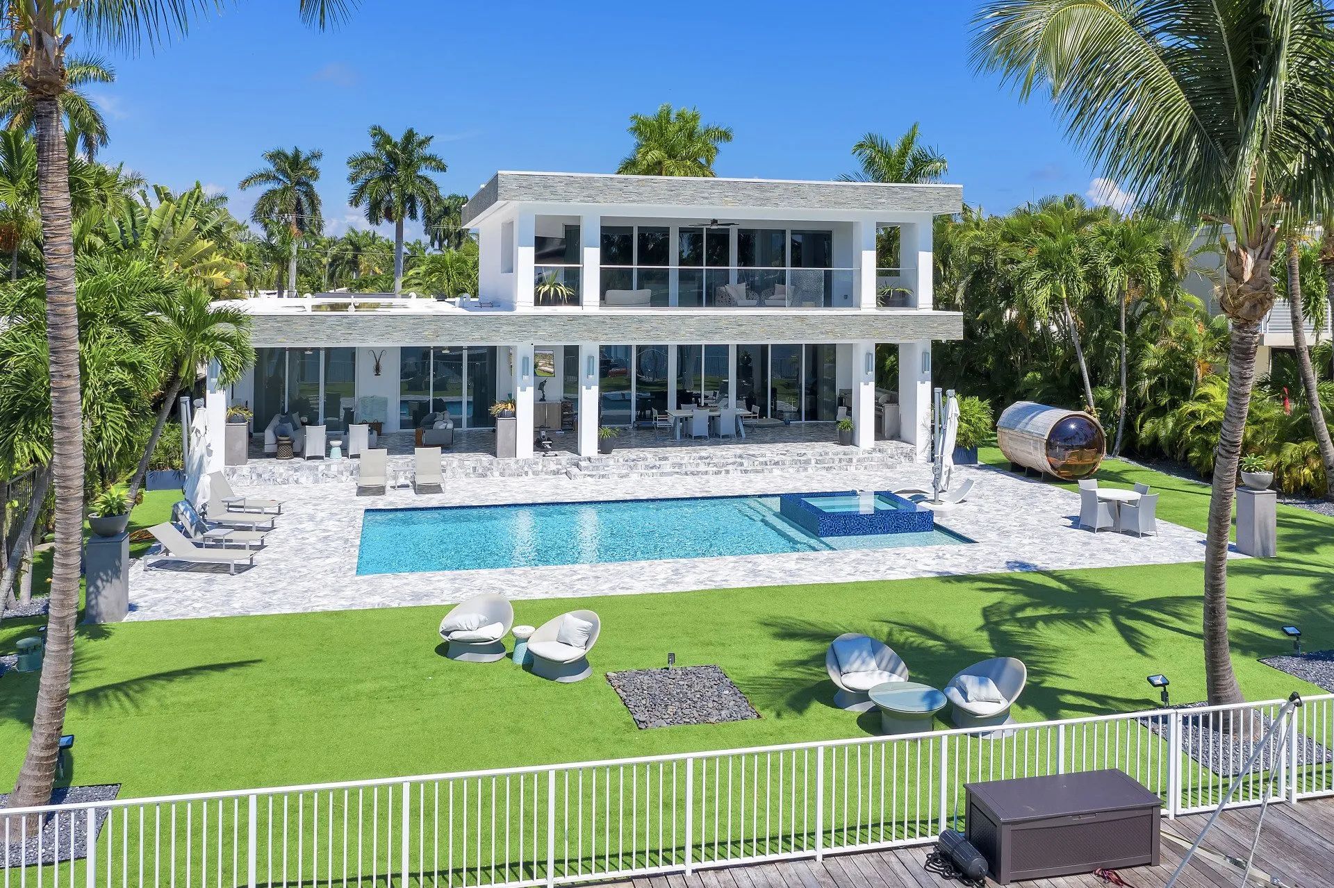 A large white house with a large swimming pool in the backyard surrounded by palm trees.