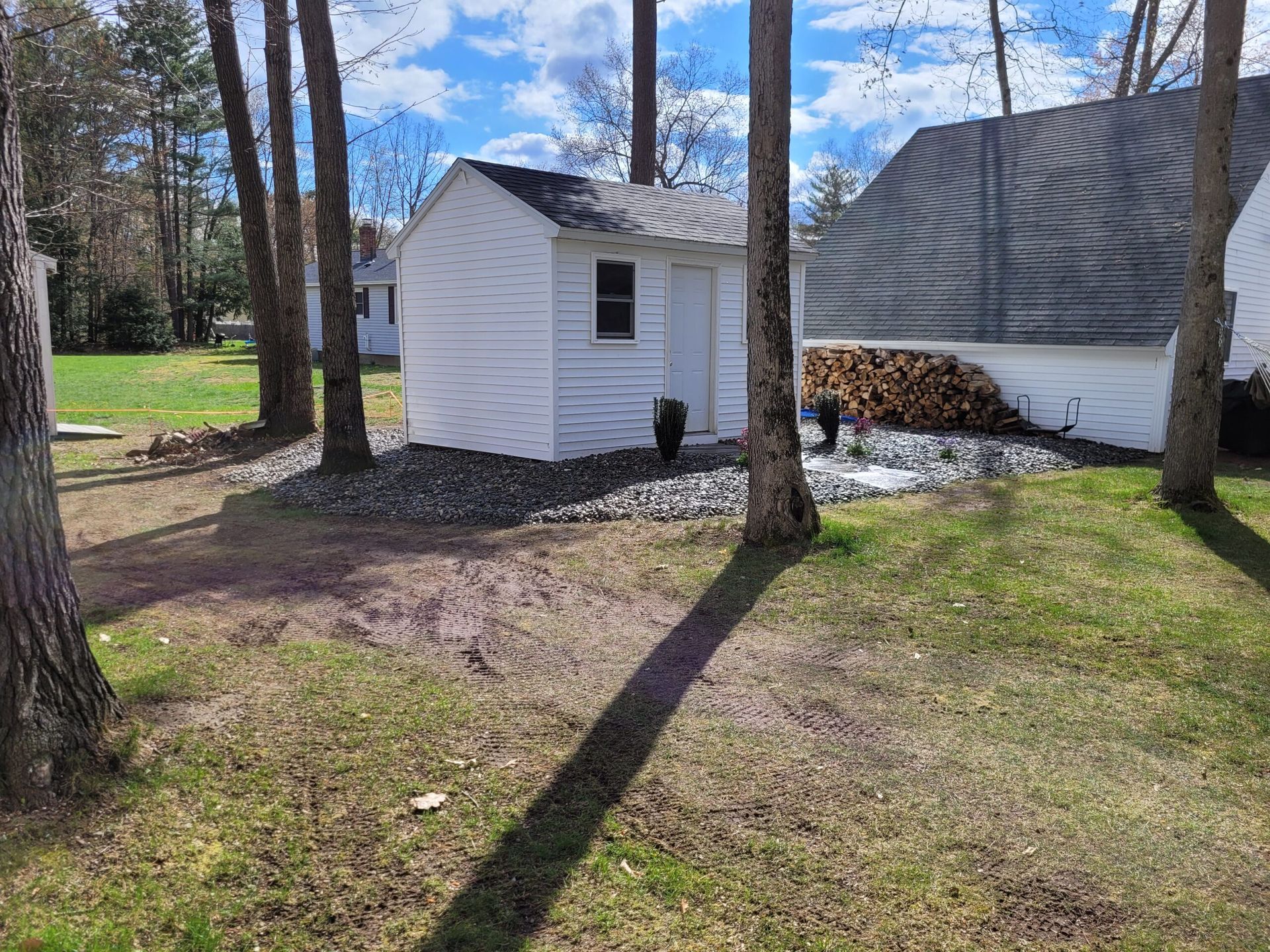 A small white shed is sitting in the middle of a lush green yard surrounded by trees.