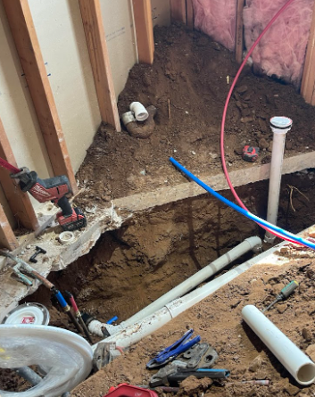 Construction site with exposed plumbing, dirt, and tools inside a bathroom.