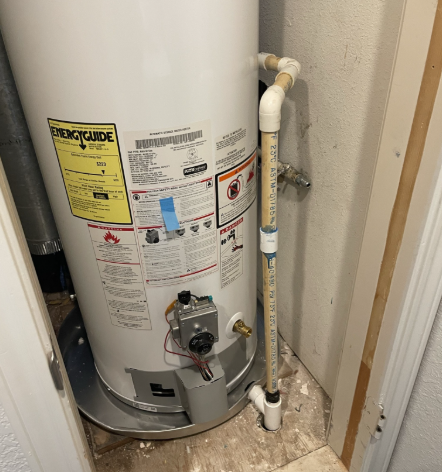 Water heater in a closet with a PVC pipe drain extending to the floor.