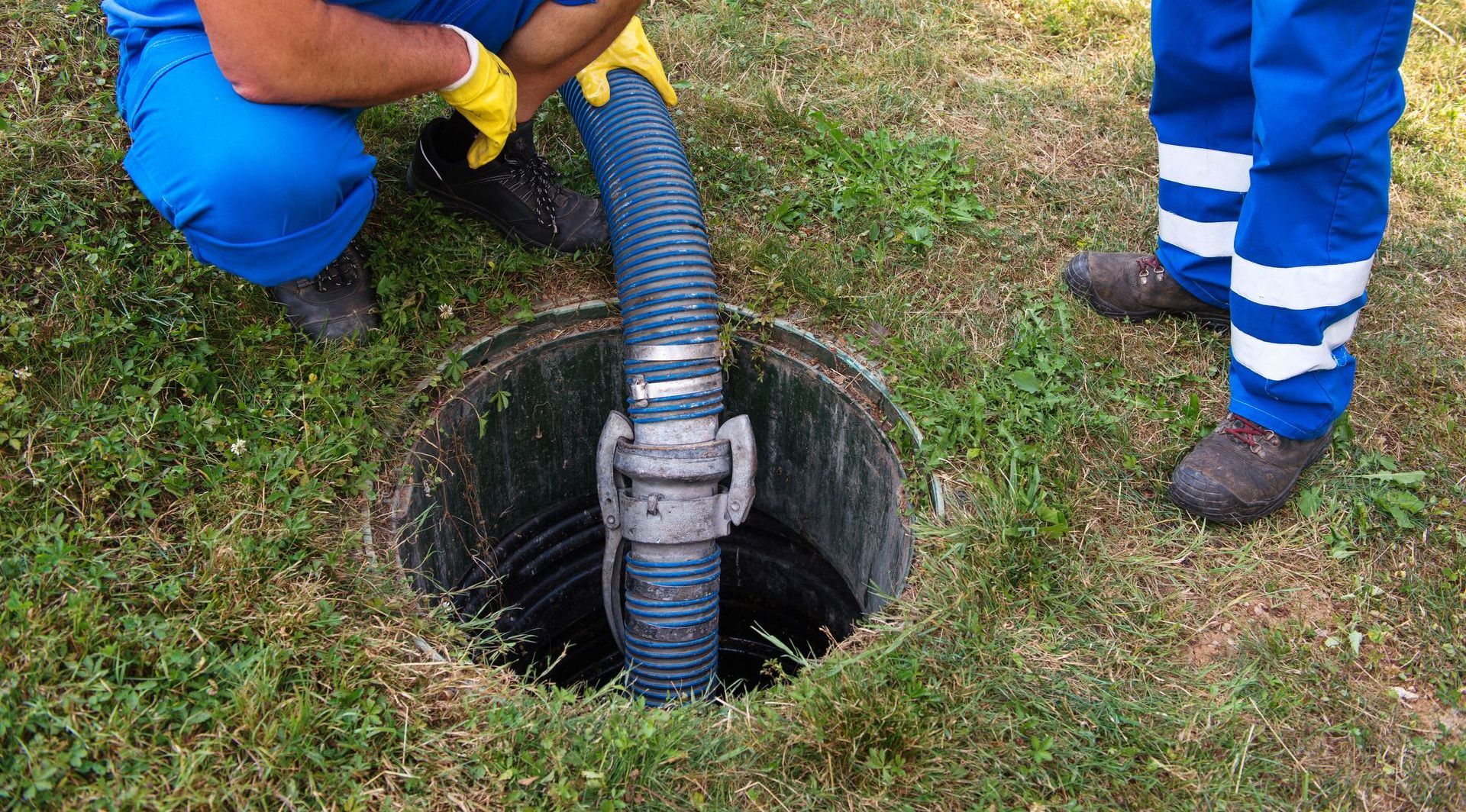 A man is pumping water into a septic tank with a hose.