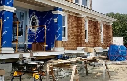 A man is standing on a scaffolding in front of a house under construction.