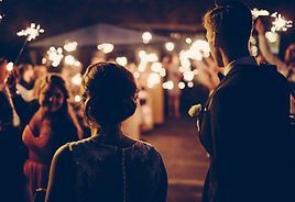 Couple walking through sparkler exit at nighttime wedding reception.