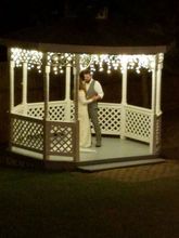 Couple dancing in a white gazebo with string lights at night.