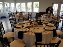 Round tables set for an event with white linens, navy napkins, and cream chairs. Two people setting up.