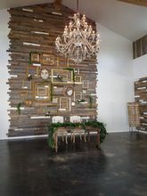 Wooden wall backdrop with frames, greenery-laden sweetheart table, and chandelier in an event space.