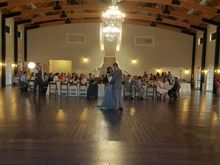 Couple dances during a wedding reception in a large ballroom with guests seated at tables.