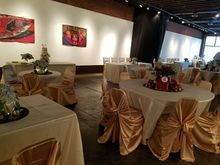 Wedding reception hall with draped tables and chairs in gold, art on the white walls.