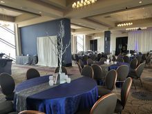 Elegant ballroom set for an event; round tables with blue tablecloths, silver runners, and centerpieces; blue walls.