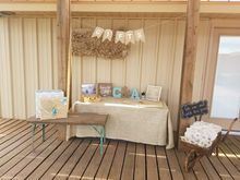 Crafts table with burlap tablecloth, banner, and decorative items. Outdoors, wooden deck.