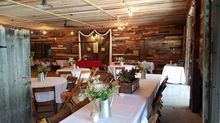Rustic interior with tables set for an event; wood-paneled walls and ceiling, string lights, flowers.