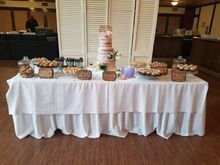 Dessert table with tiered cake, pastries, and treats, decorated in white and pink.