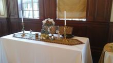 Table set with candles, flowers, and decorative items. Dark wood paneling and a window in the background.