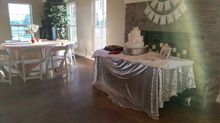 Wedding reception venue with cake on a decorated table. Other tables are set. Brick fireplace in background.