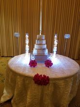 A wedding cake on a round table, lit up with surrounding decorations and flowers.