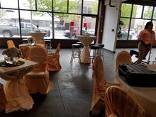 Event space with decorated tables and chairs, large windows, and a person adjusting something.