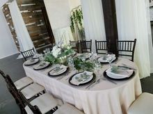Formal dining table set for event with centerpieces and place settings, surrounded by chairs and draped curtains.